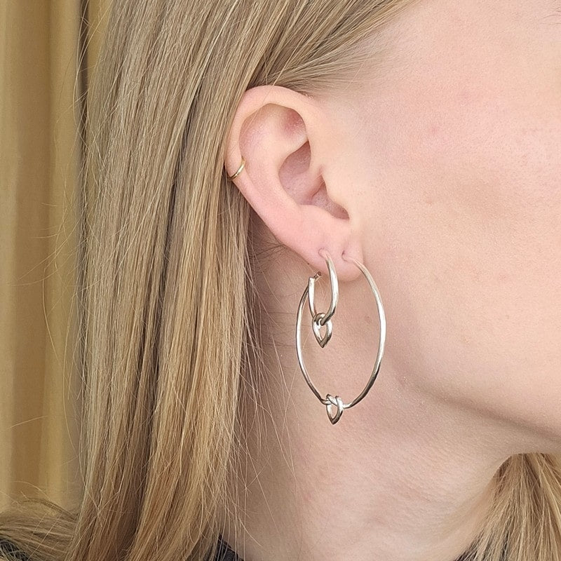 Jane Kønig Big Tied Heart Hoop øreringe i sterlingsølv, liggende på flade