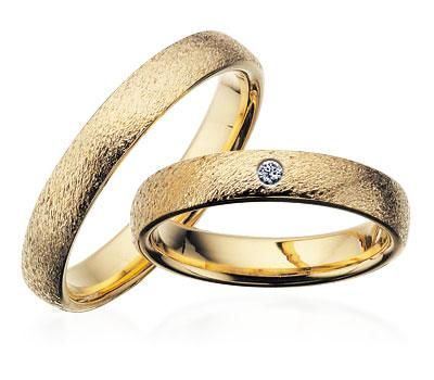 Scrouples vielsesringe i guld med rustik overflade og diamant, liggende på flade