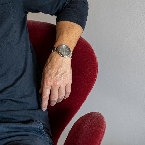 Arne Jacobsen Bankers 50års jubilæumsur i rustfrit stål med grå marmorinspireret skive, set fra siden